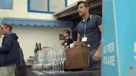 Gli ospiti con i calici in mano davanti al banco dell'aperitivo, sotto l'insegna Ali per volare dell'eliporto
