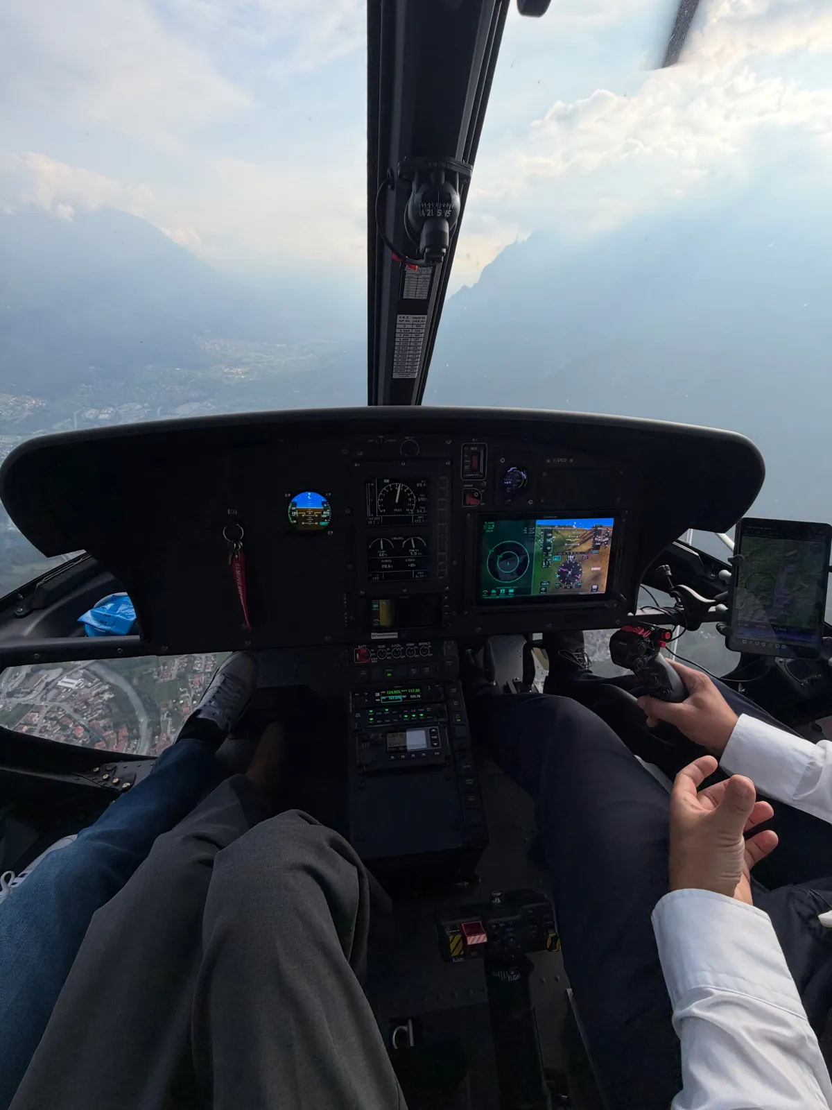 La cabina di pilotaggio in volo: strumenti accesi, le mani del pilota sui comandi e il fondovalle sotto di loro