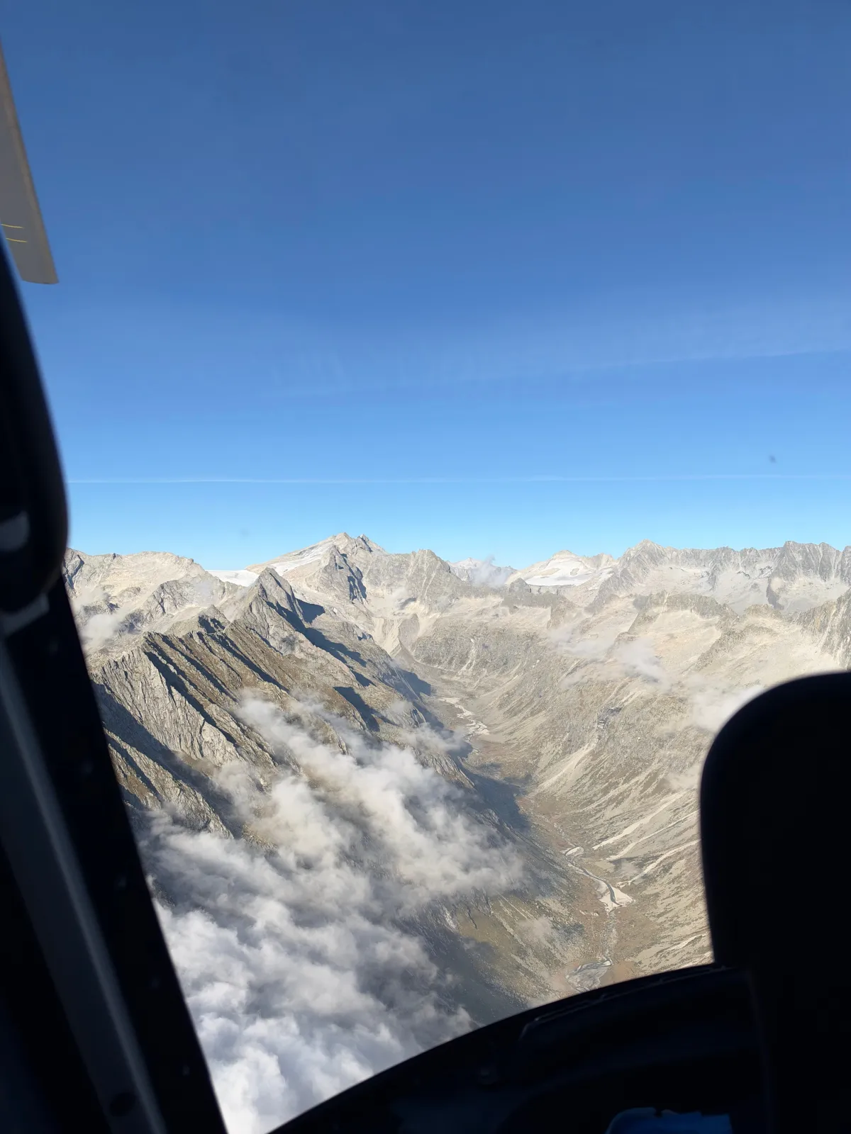 Creste rocciose e nuvole basse sotto il livello di volo, viste dall'oblò dell'elicottero